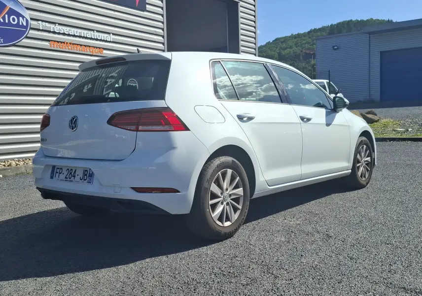 Volkswagen Golf blanc vue 3/4 arrière droit, avec jantes alliage et feux arrière LED visibles.