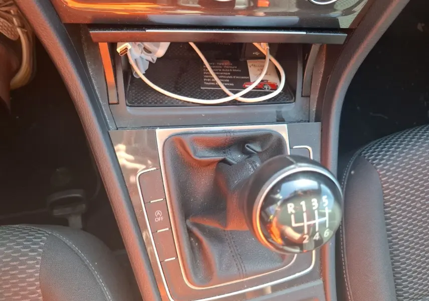 Gros plan sur le levier de vitesses manuel 6 rapports de la Volkswagen Golf blanche, avec console centrale et siège tissu visible.