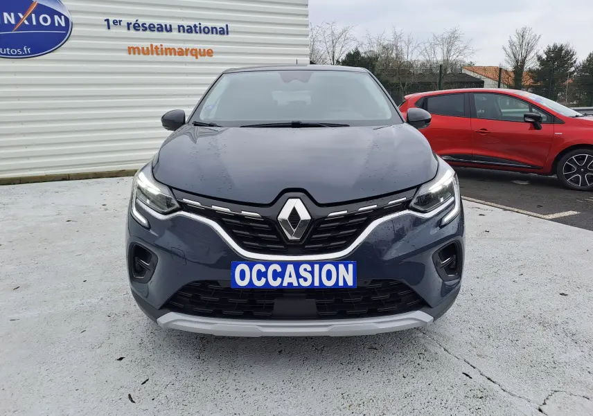 Vue avant d'un Renault Captur bleu marine 2022 avec calandre chromée et phares LED allumés sur parking.