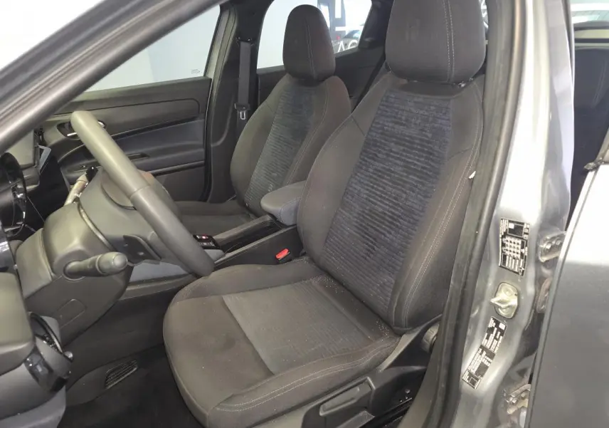 Vue intérieure côté conducteur de l'Alfa Romeo Junior 1.2 Ibrida 2025 gris, sièges tissu Icona et accoudoir central.