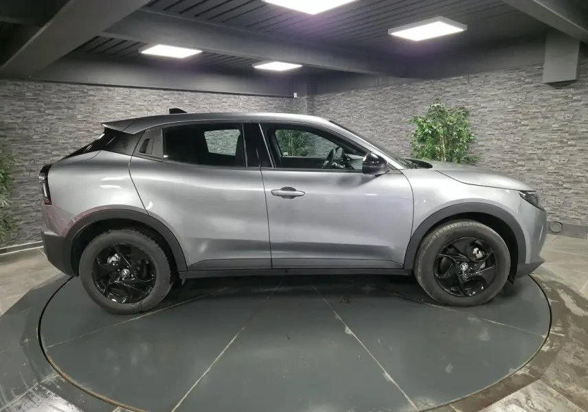 Vue de profil côté gauche d'une Alfa Romeo Junior 1.2 hybride gris métallisé avec jantes alliage noires dans un showroom.