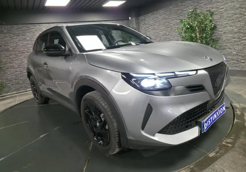 Vue 3/4 avant droite d'une Alfa Romeo Junior 1.2 hybride gris métallisé avec jantes noires et feux LED allumés.