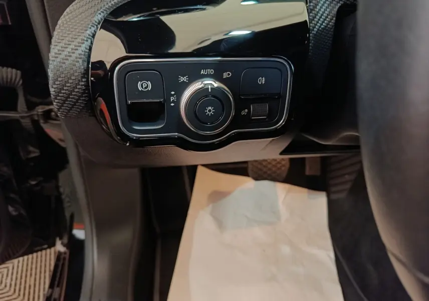 Gros plan sur le panneau de commande des feux et frein à main électrique, intérieur noir de la Mercedes Classe A 200.