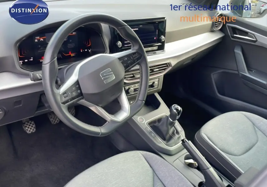 Vue intérieure de la SEAT Ibiza 2025, montrant le volant multifonction, la boîte manuelle et les sièges tissu gris.