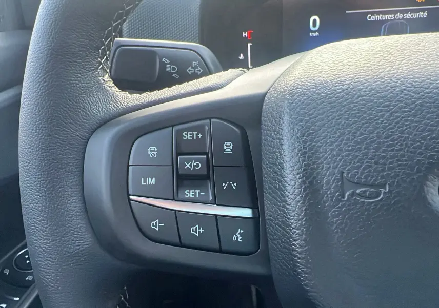 Gros plan sur les commandes multifonctions à gauche du volant cuir du Ford Ranger noir agate 2025.