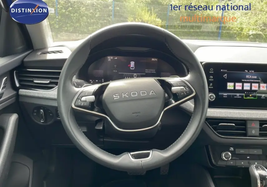 Vue intérieure centrée sur le volant SKODA d'une Scala 2025, avec tableau de bord digital et écran tactile multimédia.