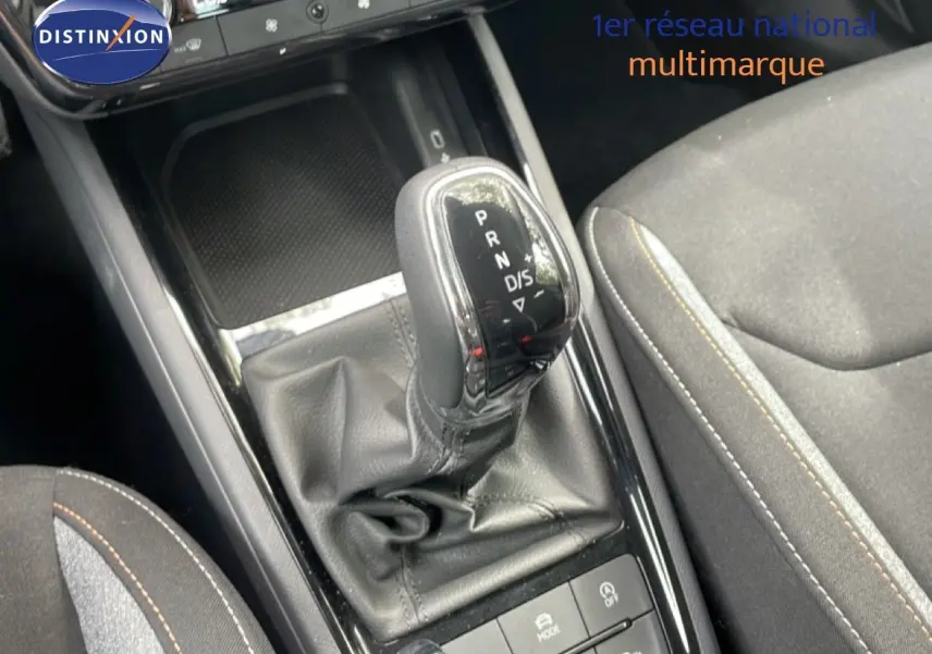 Gros plan sur la console centrale de la Skoda Scala 2025, boîte auto avec levier en cuir et sièges tissu gris noir.