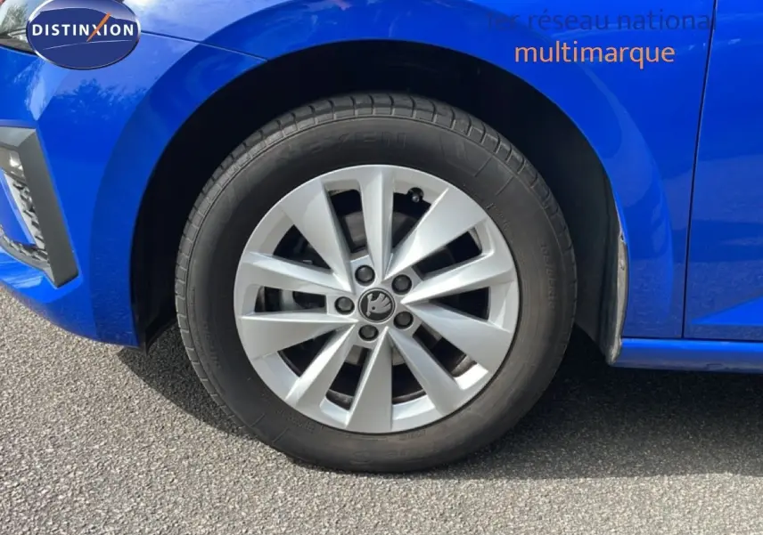 Gros plan sur la roue avant gauche d'une Skoda Scala bleu racing metal, mettant en valeur la jante argentée au design moderne.