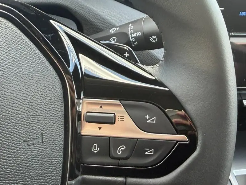 Gros plan sur les commandes au volant côté gauche du Peugeot 308 SW 2025 noir Perla Nera, avec boutons multifonctions.