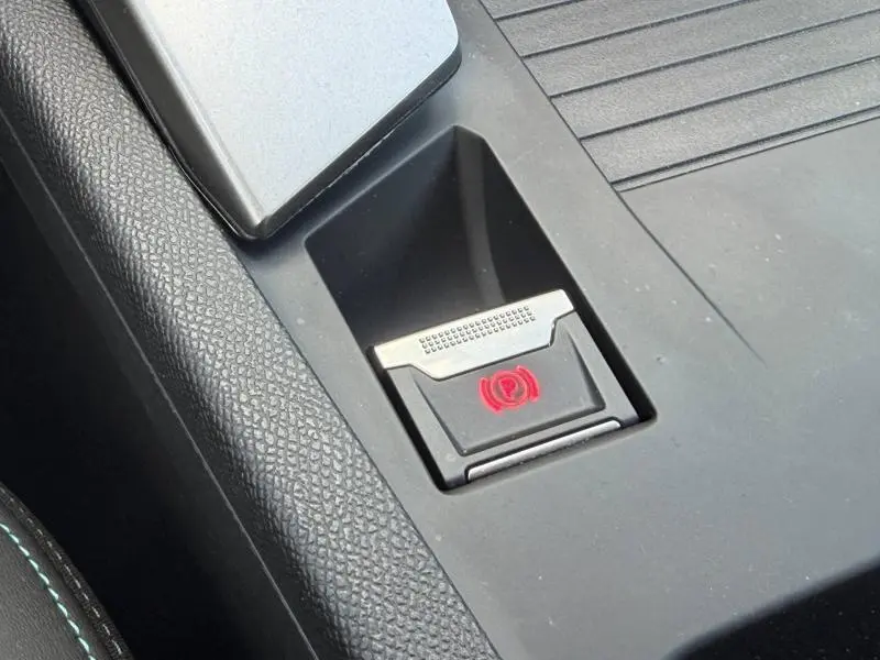Gros plan sur le bouton de frein à main électronique rouge dans l'habitacle noir du Peugeot 308 SW 2025.