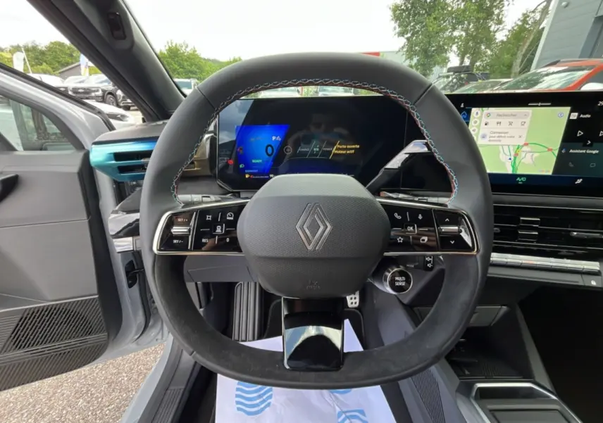 Vue intérieure centrée sur le volant cuir noir avec surpiqûres tricolores et tableau de bord numérique de la Renault Clio Gris Rafale.