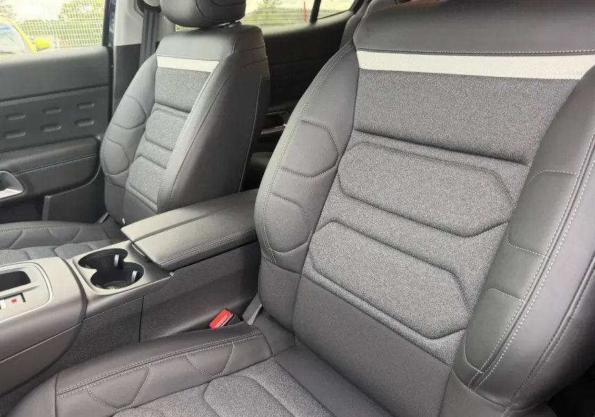 Vue intérieure rapprochée des sièges avant en tissu noir et cuir avec accoudoir central du Citroën C5 Aircross 2025.