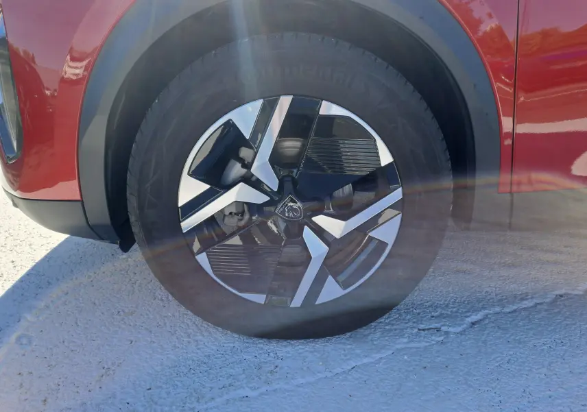 Gros plan sur la roue avant gauche du Peugeot 2008 rouge Elixir, mettant en valeur la jante au design moderne bicolore.
