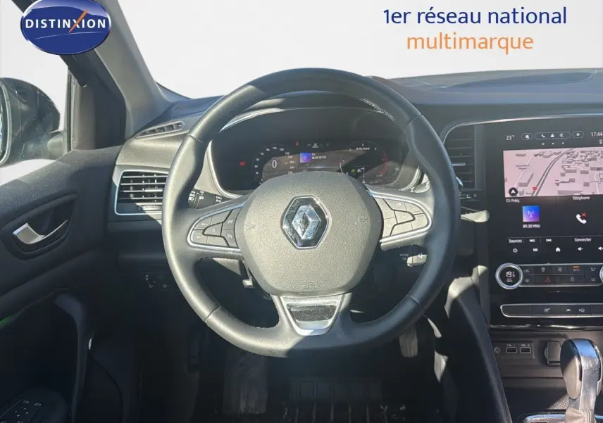 Vue intérieure centrée sur le volant et tableau de bord d'une Renault Mégane Break gris titanium 2024 avec écran tactile et boîte auto.