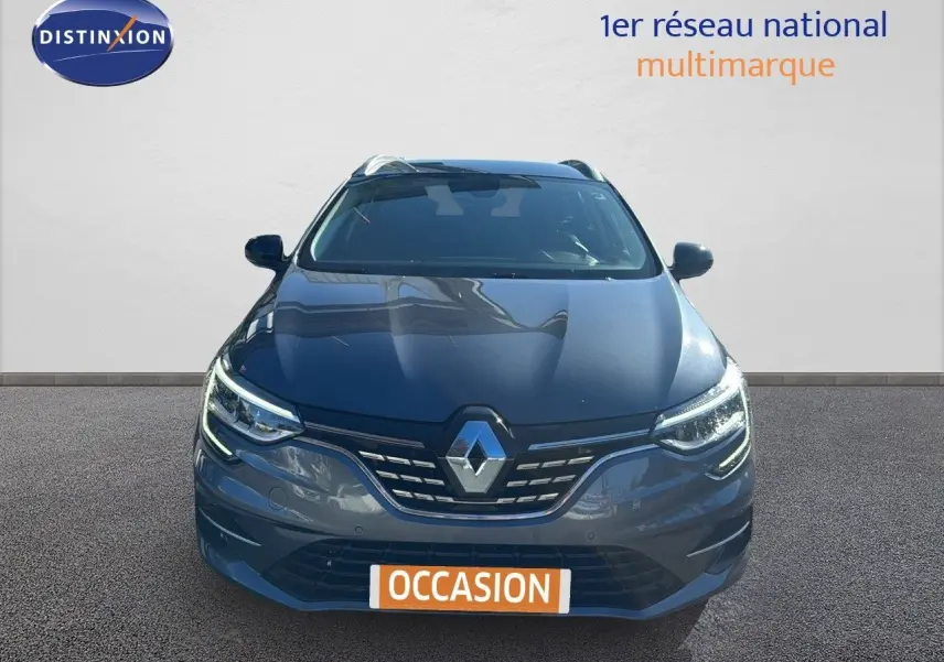 Vue avant d'une Renault Mégane Break gris titanium métal avec calandre et phares LED allumés sur fond neutre.