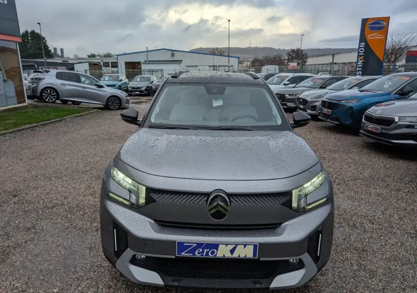 Vue avant d'un Citroën C3 Aircross gris métallisé avec toit noir et phares LED allumés sous la pluie.