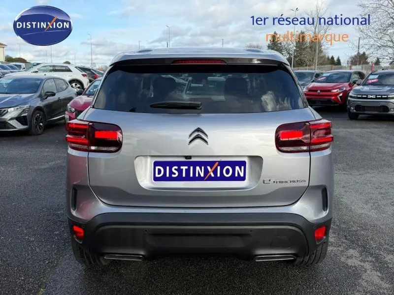 Vue arrière d'un Citroën C5 Aircross gris 2024 avec feux rouges et logo distinctif sur un parking multimarque.