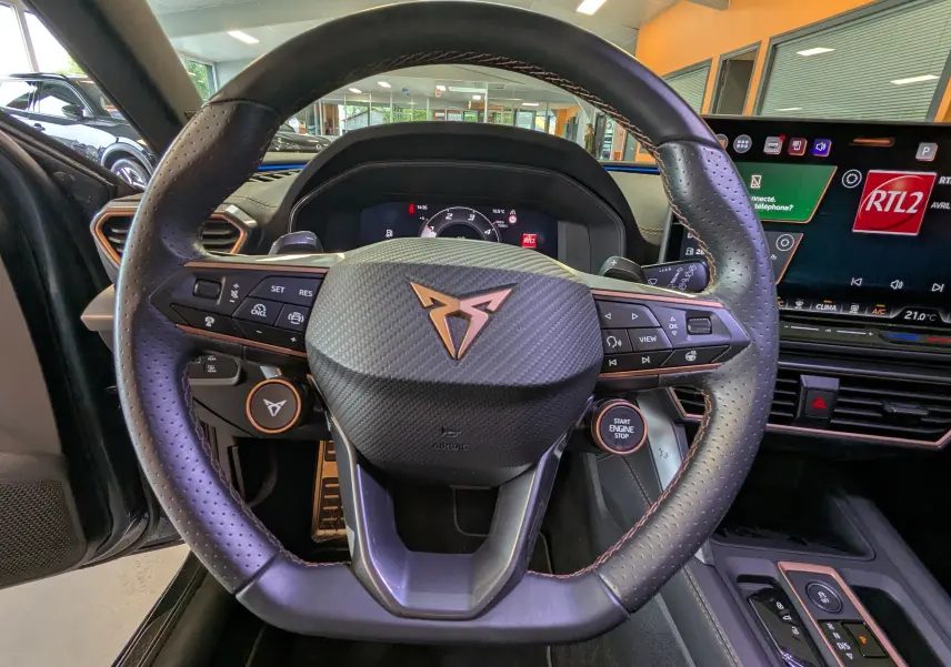 Vue centrée sur le volant perforé noir avec logo CUPRA cuivré, tableau de bord numérique et écran tactile 12,9 pouces.