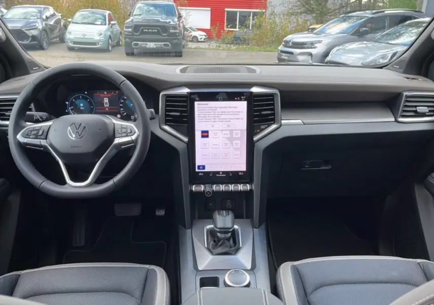 Vue intérieure avant du Volkswagen Amarok Simple Cabine 2025, tableau de bord moderne avec écran tactile vertical et volant cuir noir.