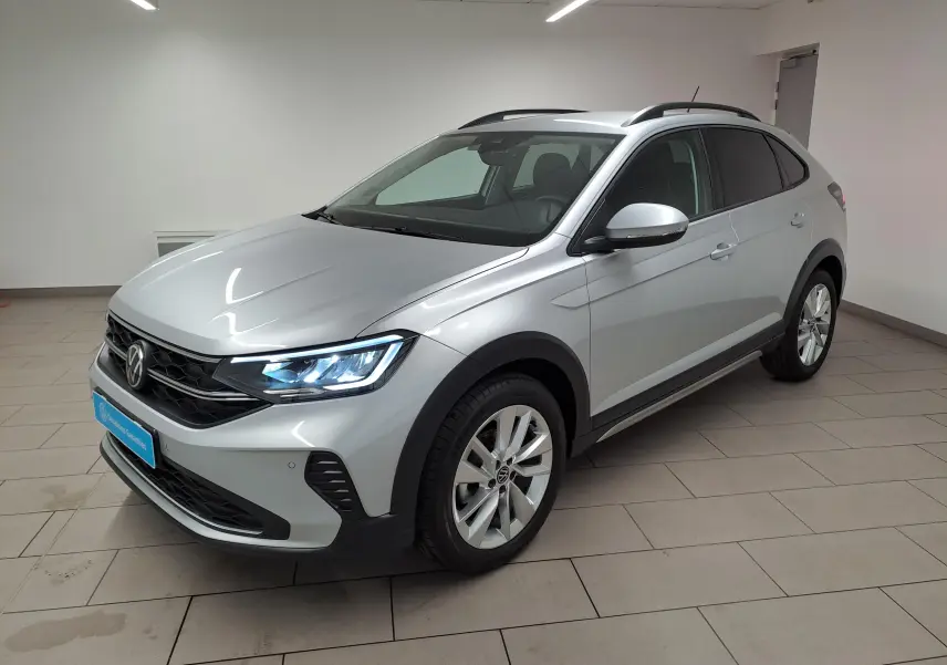 Volkswagen Taigo 2025 en Reflet d'argent, vue 3/4 avant droit avec phares allumés et jantes alliage.