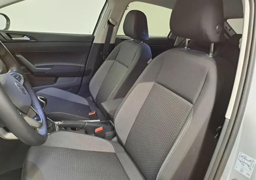 Vue intérieure côté conducteur du Volkswagen Taigo 2025, sièges tissu gris avec détails noirs, volant partiellement visible.