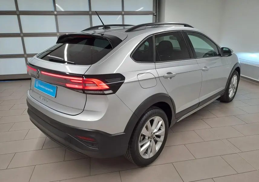 Vue 3/4 arrière droite du Volkswagen Taigo 2025 en peinture métallisée Reflet d'argent avec feux arrière allumés.