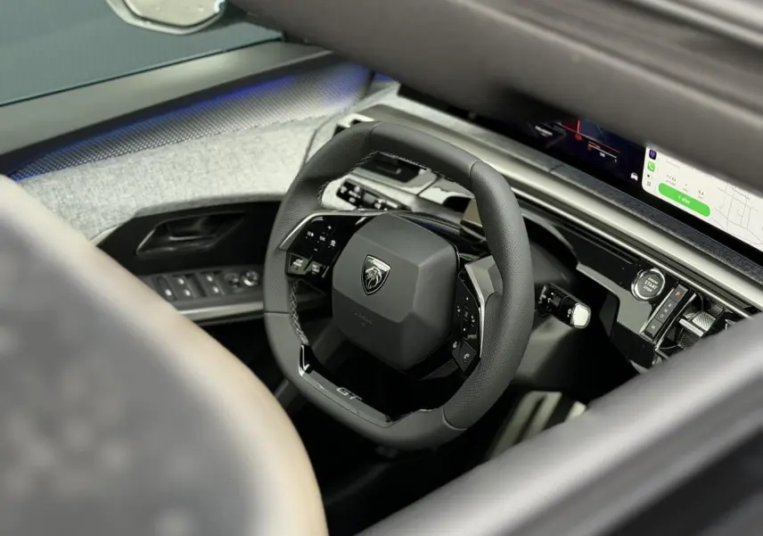 Vue intérieure rapprochée du volant compact cuir noir GT du Peugeot 3008 Hybrid 2026 avec tableau de bord numérique incurvé.