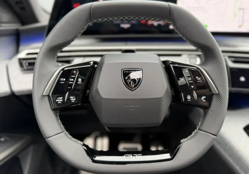 Volant compact cuir perforé gris avec badge GT au centre du tableau de bord du Peugeot 3008 Hybrid 2026.