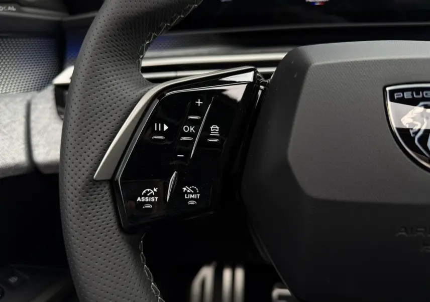 Gros plan sur le volant cuir perforé noir du Peugeot 3008 Hybrid GT avec commandes intégrées et logo Peugeot central.