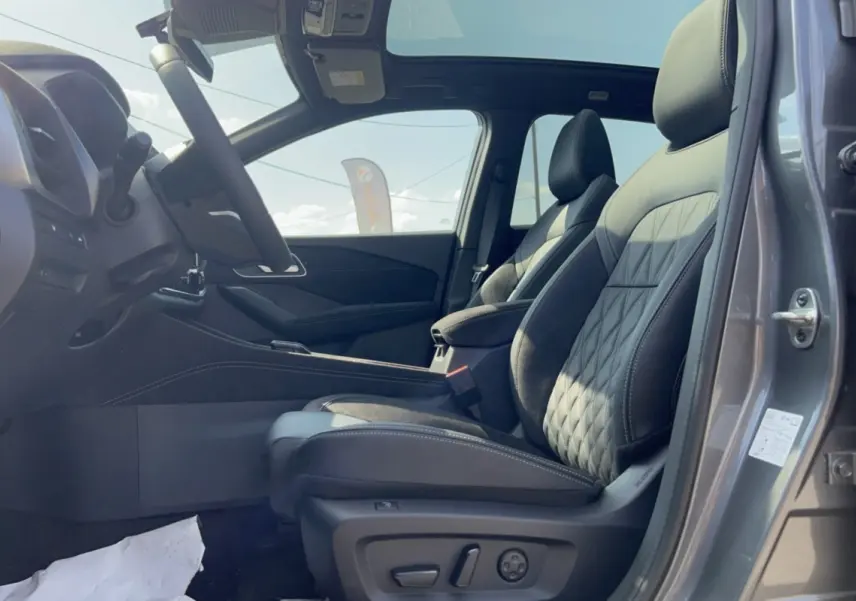 Vue intérieure côté conducteur du Nissan Qashqai E-POWER 205 Tekna Plus gris squale, sièges cuir avec surpiqûres et toit panoramique visible.
