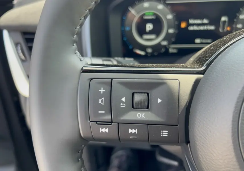 Gros plan sur les commandes multifonctions à gauche du volant cuir du Nissan Qashqai gris squale, tableau de bord en arrière-plan flou.