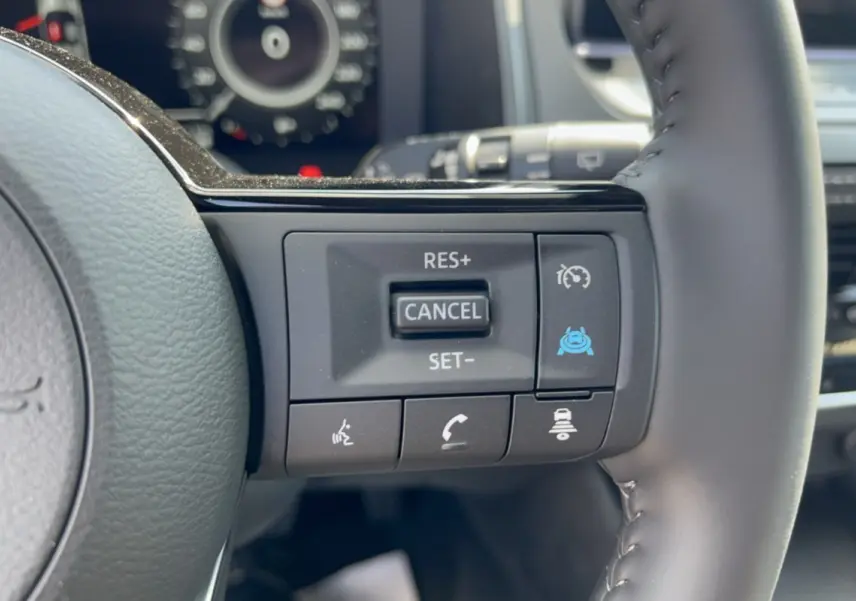 Gros plan sur les commandes multifonctions du volant cuir du Nissan Qashqai E-POWER 205 Tekna Plus, intérieur noir.
