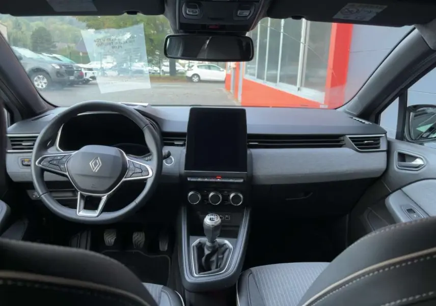 Vue intérieure avant de la Renault Clio gris rafale 2025, avec volant multifonctions et écran tactile vertical central.