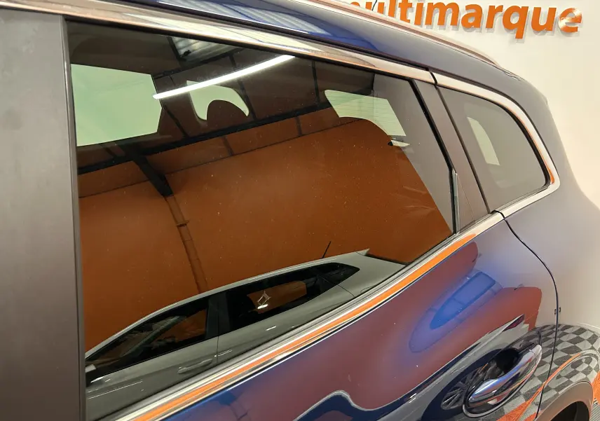 Gros plan sur la porte arrière côté droit d’un Renault Kadjar bleu 2017 avec reflet d’un autre véhicule blanc.
