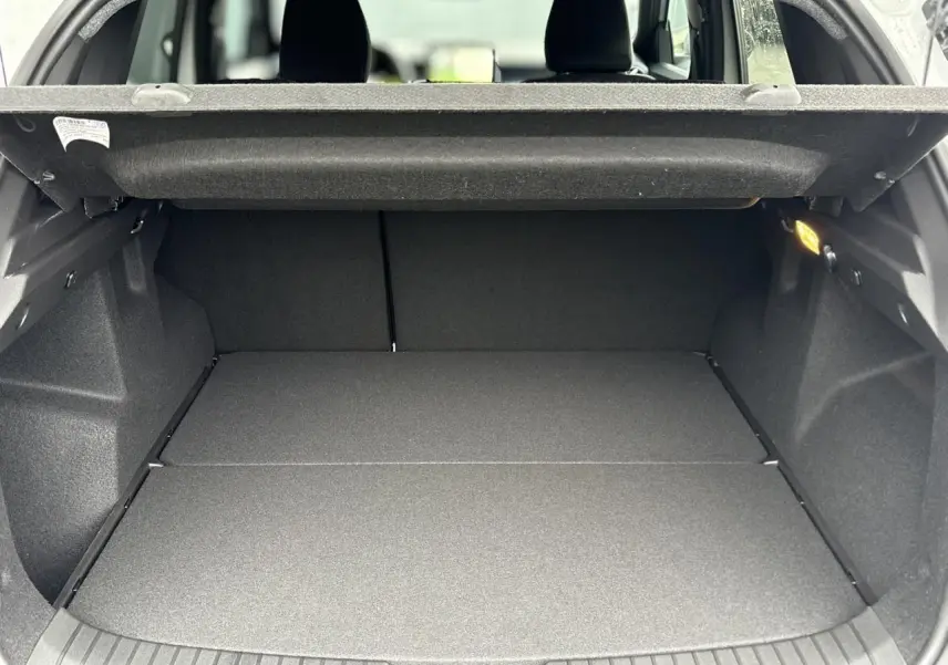 Coffre spacieux ouvert du Dacia Duster blanc Glacier 2025, montrant la banquette arrière rabattue et le revêtement noir.