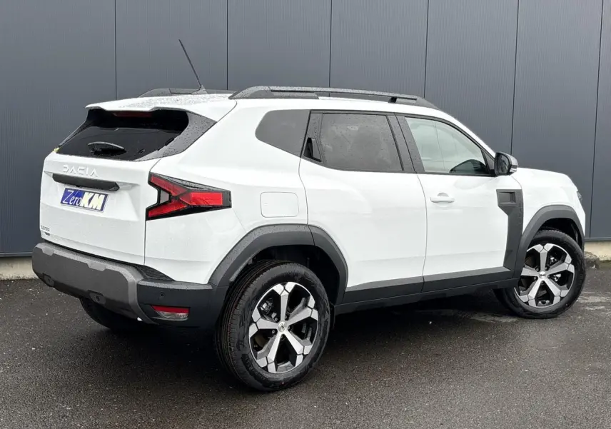 SUV Dacia Duster blanc glacier vu en 3/4 arrière droit, avec jantes alliage et barres de toit noires.