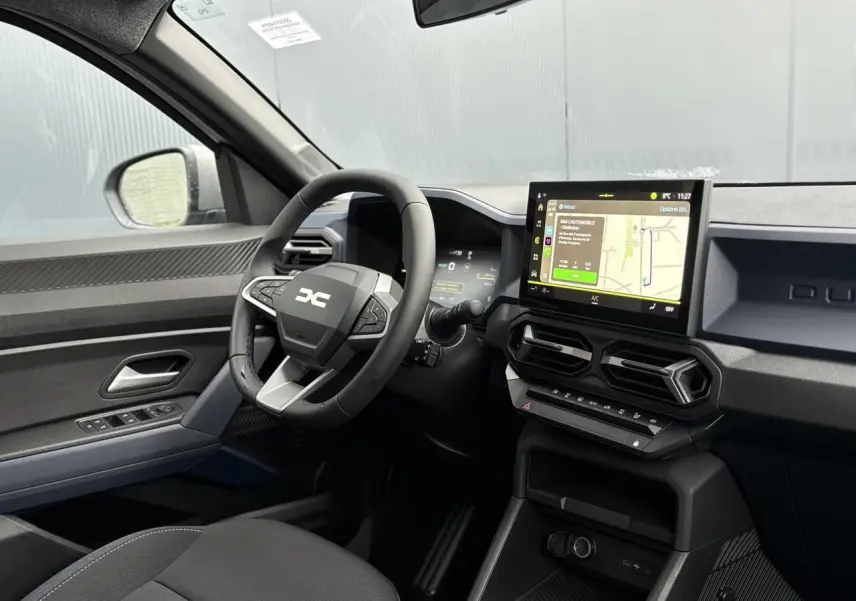 Intérieur du Dacia Duster 2025 côté conducteur, tableau de bord noir avec écran tactile GPS et volant multifonction.