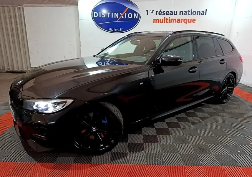 BMW Série 3 318i M Sport noire vue en 3/4 avant droit avec jantes noires et phares allumés dans un showroom