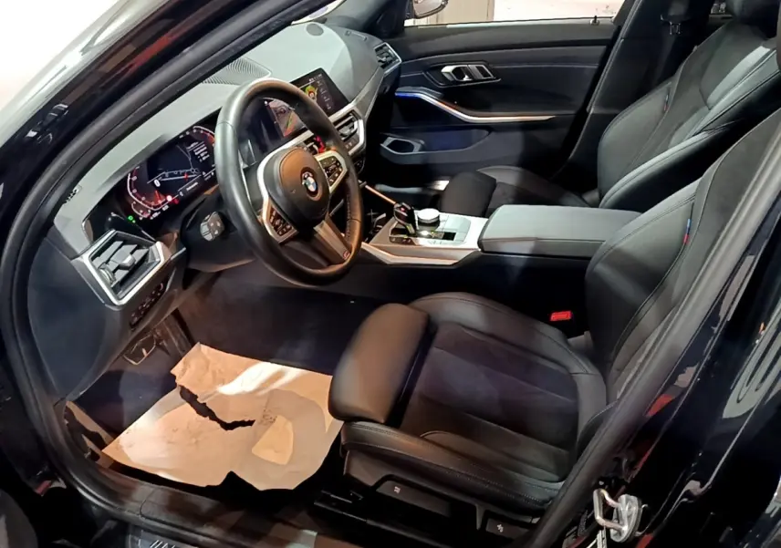 Intérieur noir de BMW Série 3 318i 2022, vue côté conducteur montrant sièges cuir et tableau de bord digital.
