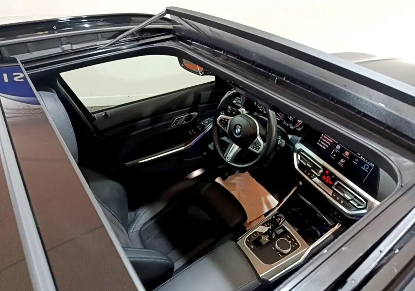 Vue intérieure par le toit ouvrant d'une BMW Série 3 noire, mettant en valeur le tableau de bord digital et le volant cuir.