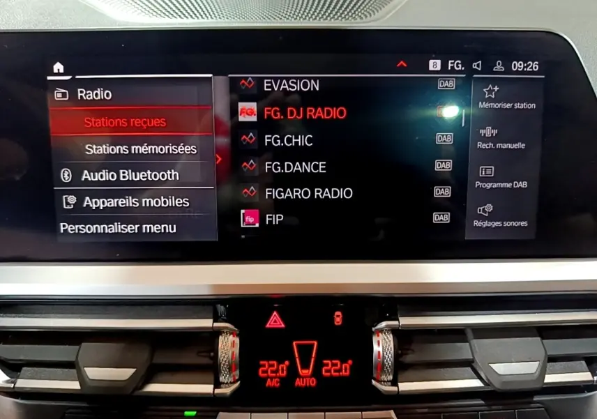 Vue rapprochée de l'écran tactile central et commandes de climatisation rougeoyant d'une BMW Série 3 noire 318i M Sport 2022.