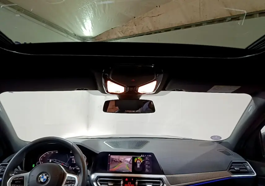 Vue intérieure avant du tableau de bord et volant cuir d’une BMW Série 3 318i noir avec écran tactile et éclairage d’ambiance bleu.