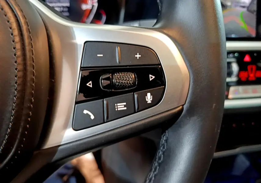 Gros plan sur les commandes du volant en cuir noir de la BMW Série 3 318i M Sport 2022 avec tableau de bord en arrière-plan.