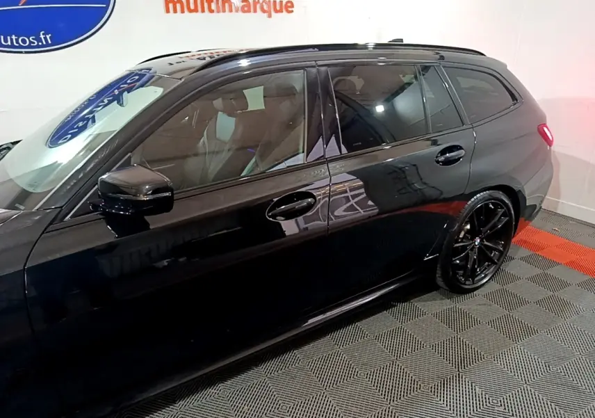 Profil côté gauche d'une BMW Série 3 noire 318i M Sport avec jantes noires et vitres teintées en intérieur showroom.