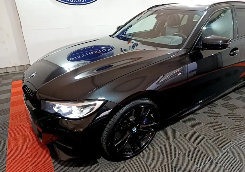 BMW Série 3 318i M Sport noir vue 3/4 avant droit avec jantes noires et phares LED allumés.