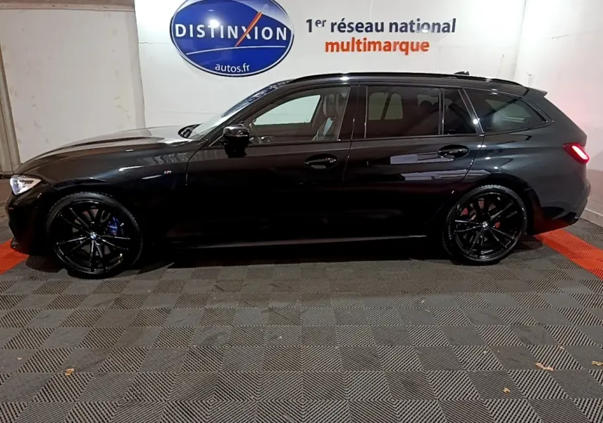 BMW Série 3 318i M Sport noir vue de profil côté gauche, avec jantes noires et feux arrière allumés dans un garage.
