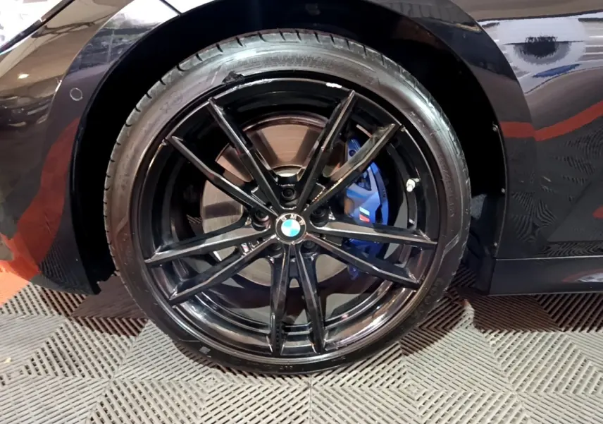 Gros plan sur la roue arrière gauche noire d'une BMW Série 3 318i M Sport avec étrier de frein bleu visible.