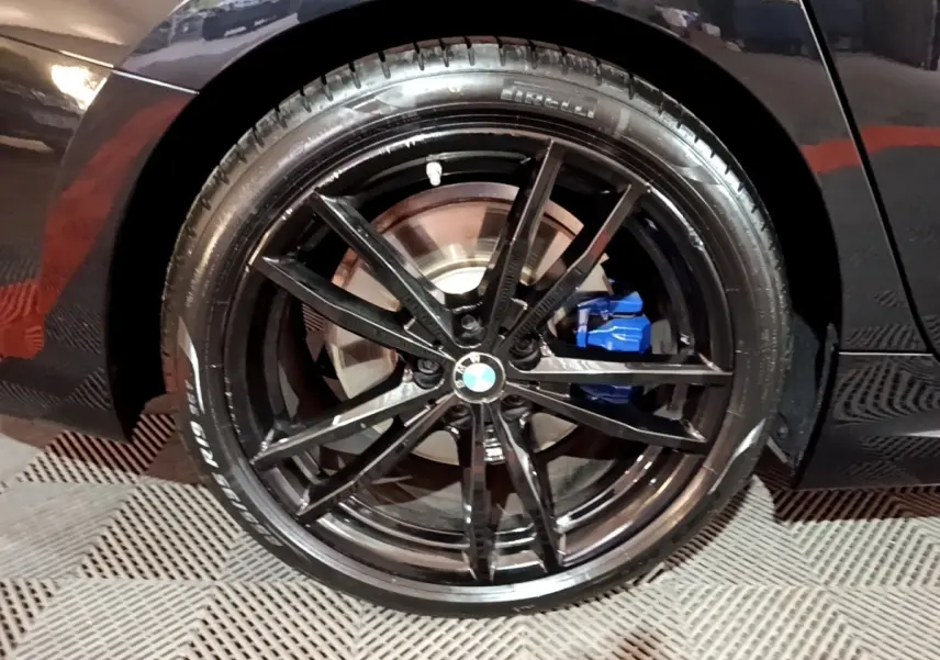 Gros plan sur la jante noire brillante et l'étrier de frein bleu de la BMW Série 3 noire côté arrière droit.