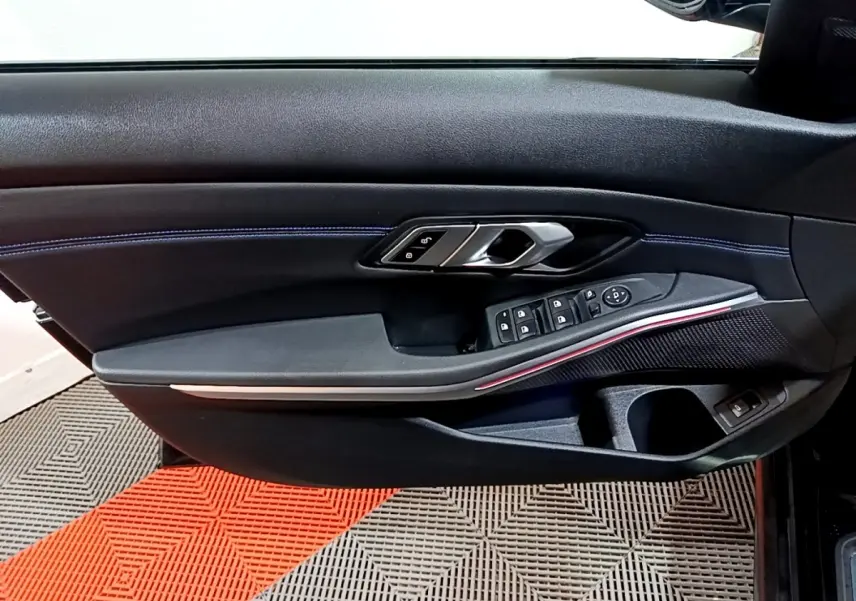 Vue rapprochée de la porte côté gauche noire de la BMW Série 3 318i M Sport avec surpiqûres bleues et commandes électriques.