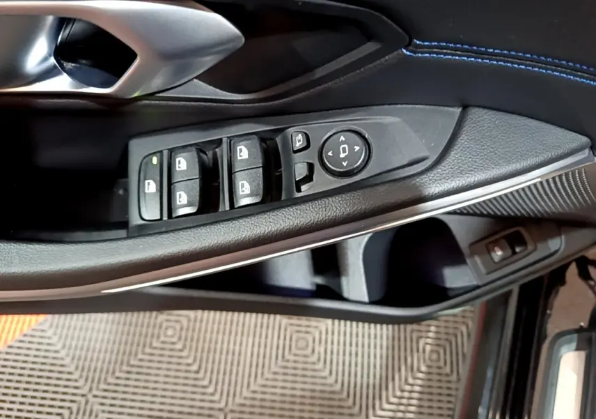 Gros plan sur la commande des vitres et rétroviseurs côté conducteur d’une BMW Série 3 noire avec surpiqûres bleues.